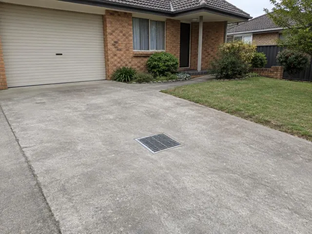 Concrete driveway with a square drain grate outside a brick house in St Clair