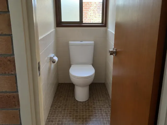 Clean toilet in a small tiled bathroom with a window and timber door in Colyton