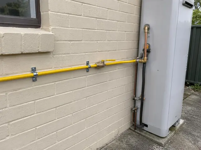 Yellow gas pipe and fittings beside an exterior wall next to a hot water unit in Erskine Park