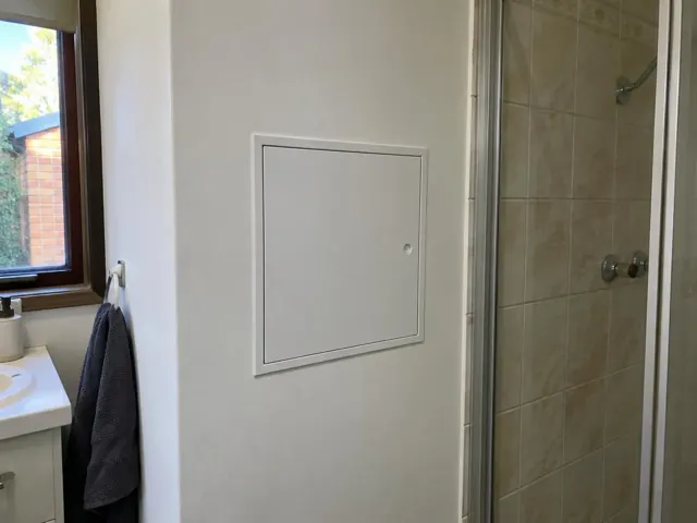 Bathroom wall with a small square access panel beside a shower and vanity in St Marys